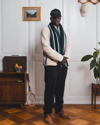 Man wearing a scarf, fleece jacket, and fleece pants is standing in front of a vintage scene