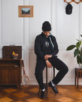 Man sitting on a vintage wooden chair in front of a white wall with a painting, a teak sideboard, and a plant