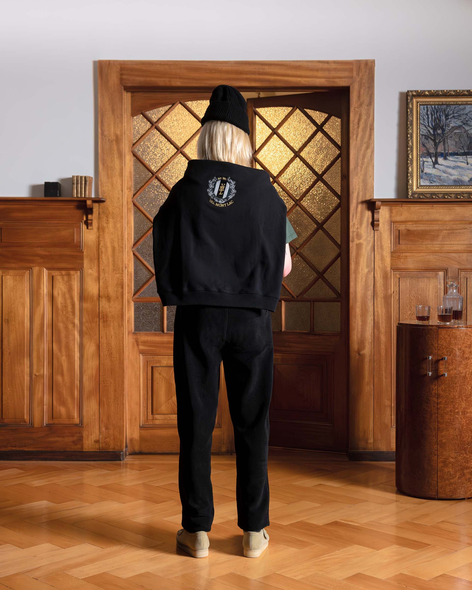 Frauenansicht von hinten, stehend mit einem schwarzen Alpime Emblem Crewneck Sweatshirt auf ihren Schultern